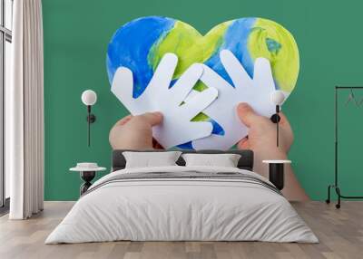 The Concept of DIY and children creativity. Step by step instruction: make applique from paper. Step 4 The child hands holds a finished craft Planet earth in the form of a heart. World Earth Day Wall mural