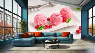 Three scoops of sweet homemade berry ice cream or refreshing sorbet of pink color decorated with juicy raspberries and fresh mint leaf served on plate on white wooden table with metal scooper utensil Wall mural