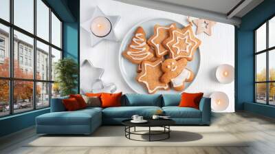 Top view of homemade spiced baked gingerbread cookies or crunchy biscuits cooked with ginger spice decorated with sweet sugar icing served on plate on white wooden background with glowing candles Wall mural