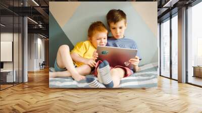 two boys in yellow and blue t-shirts sit and look at a computer tablet Wall mural