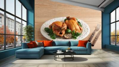 Two chicken grilled on a white plate. The greens of basil and halves of garlic were used in the preparation of chickens. There are cutlery nearby. Fresh wooden background.  Wall mural