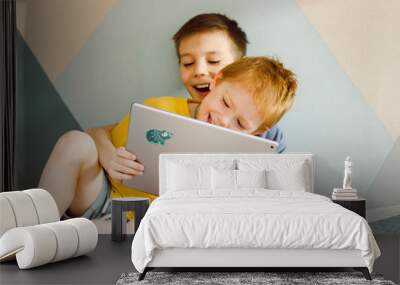 two children are sitting at home looking at a computer tablet and laughing Wall mural