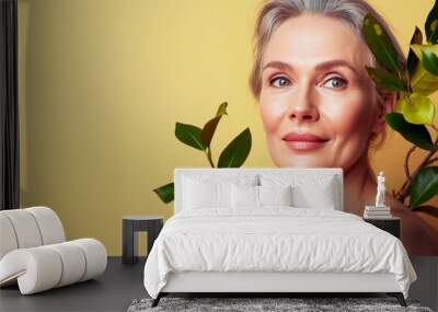 Close up shot of beautiful mature woman applying face cream on cheek while posing nude against yellow color background. Beauty care concept. Cosmetic product. Natural beauty. Wall mural