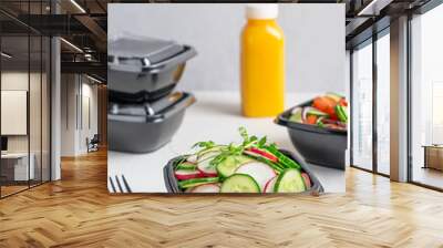 Vegetarian organic salad made of sliced cucumber and radish served in black plastic bowl with bottle of orange fruit juice and fork on white wooden table. Food delivery concept and healthy eating Wall mural