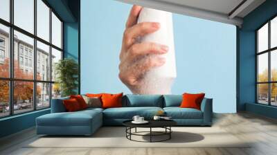 Womans hand holding cosmetics bottle with foam bubbles on pastel blue background. Bath accessories for body care, spa beauty treatment and skincare concept. Vertical, close up Wall mural