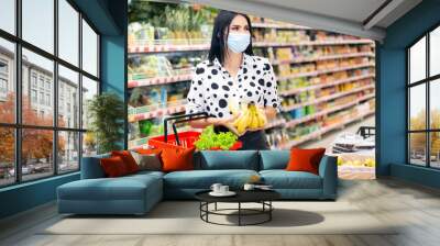 young woman in a disposable medical mask is shopping at the supermarket. buying fruit Wall mural