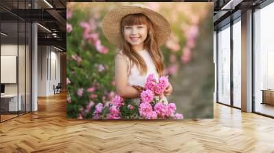 A little girl with beautiful long blond hair, dressed in a light dress and a wreath of real flowers on her head, in the garden of a tea rose Wall mural