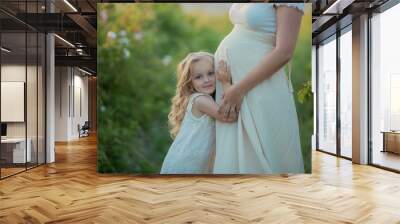 Happy pregnant woman with little daughter in a green tea rose garden Wall mural