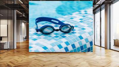 Blue professional swimming goggles with water drops on yellow lenses on a blue and white tiles of pool floor. Wall mural