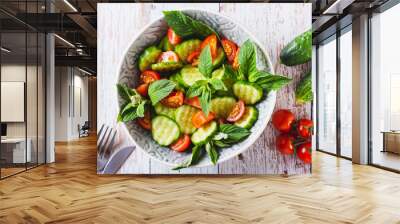 Close up of salad of cucumbers, cherry tomatoes and mint leaves in a bowl on the table top view Wall mural