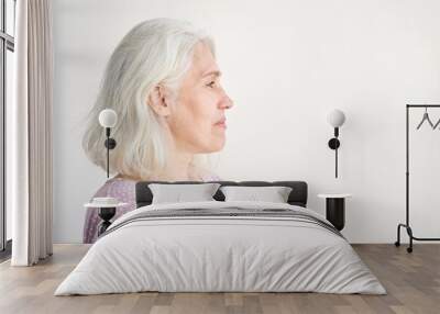 Profile of a contemplative elderly woman with gray hair in casual attire against minimalist background. Wall mural