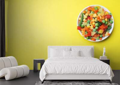 Chopped frozen vegetables in a plate on a yellow background. Corn peas pepper carrots. copy space. Wall mural