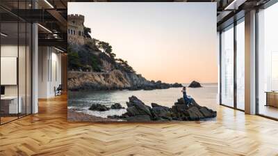 Ancient stone fortress on the seashore against the sunset. Woman sitting on a stone on the seashore. Photo Wall mural