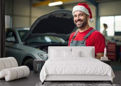 A male European auto mechanic stands in a service center in a Santa Claus hat, celebrates the new year, mechanic, repairs a car Wall mural