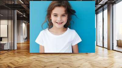 Portrait of a pretty smiling 7-year-old girl in a white T-shirt on a blue background, copy space. Happy child, childhood Wall mural