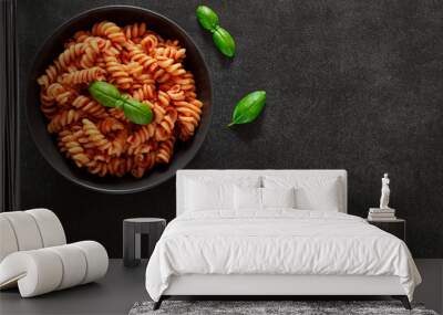 Fusilli pasta cooked with tomato sauce and basil in bowl, on dark background, top view, space to copy text. Wall mural