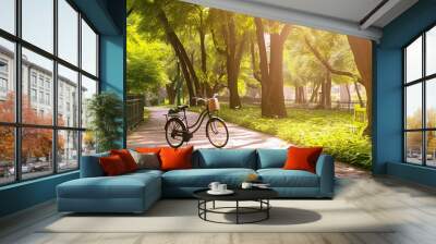 Bicycle in shade of trees with dense foliage in sun-drenched urban natural spring summer park Wall mural