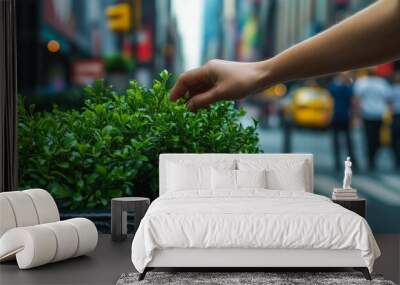 A hand gently touches a vibrant green plant nestled in a decorative pot while busy New York City pedestrians and yellow taxis are in the background Wall mural