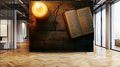 A soft glow from a lit candle illuminates an open Bible and a rosary on a rustic wooden table, inviting moments of peace and contemplation in a quiet setting Wall mural