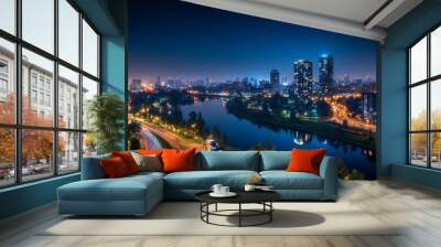 A stunning night view of a city skyline showcases twinkling lights from tall buildings and busy streets, with a river reflecting the vibrant glow against a dark sky Wall mural