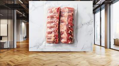 Two vacuum-sealed pork ribs neatly arranged on a white marble surface, casting shadows Wall mural