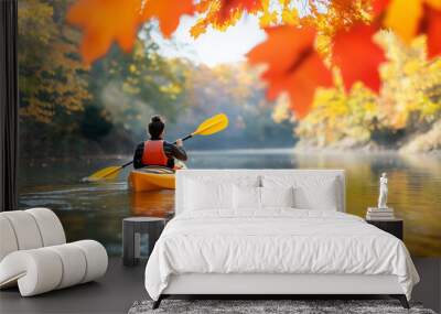 A kayaker enjoys a peaceful journey on calm waters, surrounded by vibrant fall leaves Wall mural