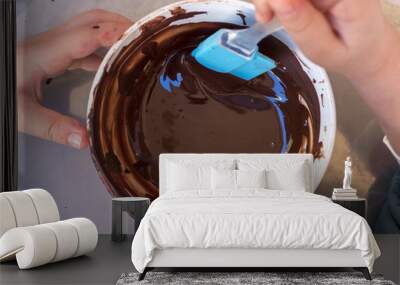 hands of a child play the pastry chef mixing chocolate in a bowl before pouring it into the chocolates molds. View from above. Wall mural