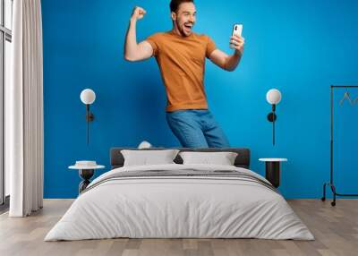 A man is jumping in the air with his arms raised and a cell phone in his hand Wall mural