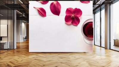 Red wine in glasses. Flat-lay of wine glasses with red wine and pink flowers petals over white background, top view, wide composition. Wine tasting, winery, bar background with copy space for text. Wall mural