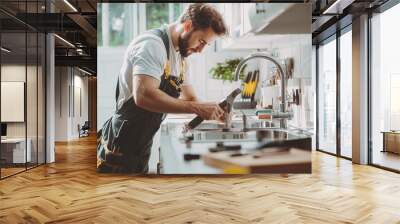 A professional plumber in dark overalls meticulously working on a kitchen faucet in a well-lit, modern home Wall mural