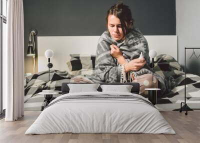 The theme is seasonal cold, runny nose flu virus infection. Young Caucasian woman at home bedroom bed sitting wrapping blanket, chill heat high temperature. Cup drink pills blister season flu Wall mural