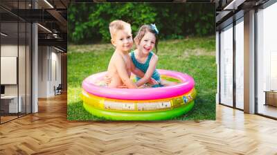 Theme is a children's summer vacation. Two Caucasian children, brother and sister, sit in a perched round pool with water in the yard of the green grass in a bathing suit and joy happiness smile Wall mural