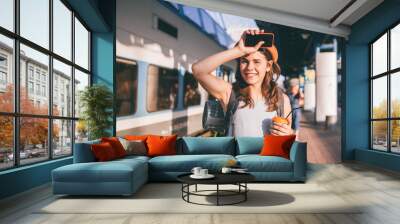 Tourism and travel in the summer. Vacations for the student. Work and travel. Caucasian young woman drinks coffee on the platform of the railway station against the background of the train Wall mural