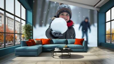 Boy holding snowball in hand, children playing snowballs outdoors in forest Wall mural