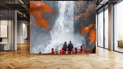 A breathtaking waterfall in autumn surrounded by red leaves and a red bridge., with two people standing together in companionship.  Wall mural