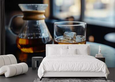 A glass of whiskey with ice sits on a black table, next to a carafe of hot coffee. Wall mural