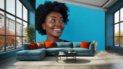 A beautiful black woman with a joyful expression gestures towards a blank space with enthusiasm Wall mural