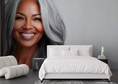 A beautiful mature black woman with glowing skin and long silver-gray hair smiles warmly, radiating confidence and elegance in a simple, neutral setting Wall mural