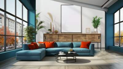 A black poster frame mockup stands on a wooden console in a modern living room with plants, a vase, and a sculpture. White wall, window in background Wall mural