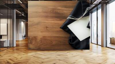 A carefully folded black cap and gown sit next to a pristine white graduation certificate on a textured wooden surface, symbolizing academic achievement and celebration Wall mural