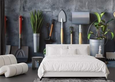 A variety of gardening tools, including shovels, rakes, and a trowel, are neatly arranged on a concrete wall. Two small potted plants and a potted tree add a touch of greenery to the scene Wall mural