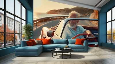 An elderly man with a beard enjoys driving a classic convertible along a breathtaking coastal road, basking in the warm glow of the sunset Wall mural