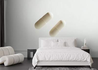 Two small white pills are suspended midair, sharply focused against a pristine white background, emphasizing their shape and texture in a minimalist composition Wall mural