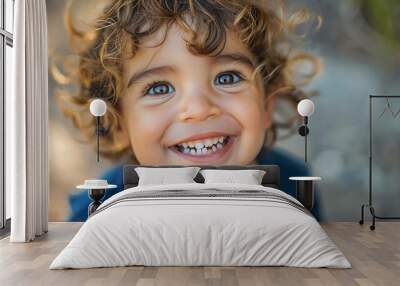 A close-up portrait of a toddler with curly hair smiling brightly. Wall mural