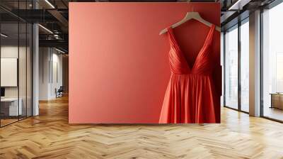 A coral-colored dress hangs on a wooden hanger against a bright red wall. Wall mural