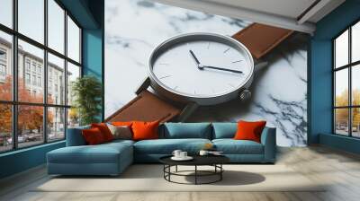 A silver wristwatch with a brown leather strap lies on a marble surface. Wall mural