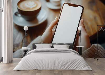 A woman holding a smartphone with a blank white screen in a cafe, with a cup of coffee in the background. Wall mural