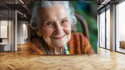 An elderly woman with a warm smile and kind eyes looks at the camera. Wall mural