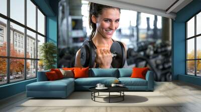 Commercial female model with perfect smile lifting weights curling dumbbell for toned fit arms Wall mural