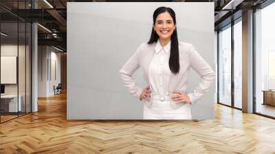 Portrait of a confident brunette business woman standing proud in suit, with her hands on hip, smiling with confidence and success on bright background Wall mural